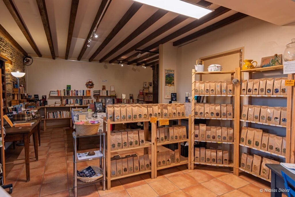 Intérieur boutique Rochefort-en-Terre avec étagères de livres et sachets de plantes.
