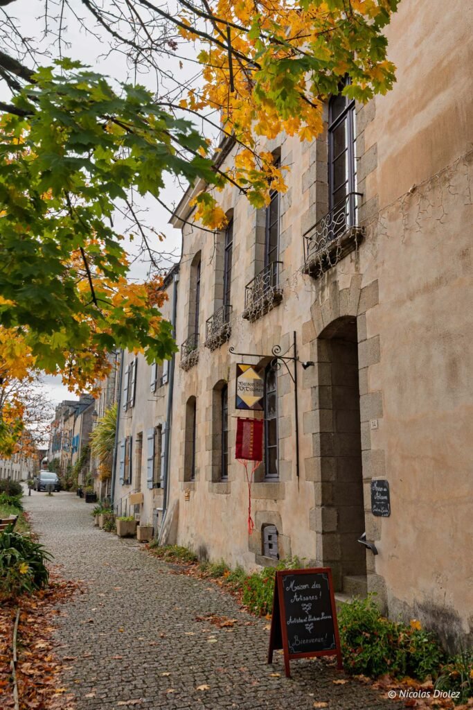 Rue pavée Rochefort-en-Terre avec Maison des Artisanes et feuilles d'automne.