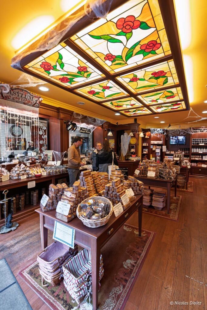 Intérieur boutique confiserie Rochefort-en-Terre avec vitraux et clients achetant des biscuits.