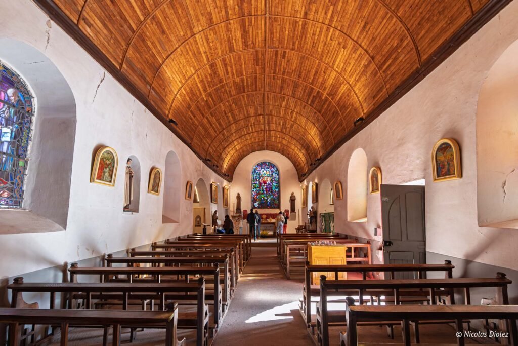 Intérieur église du Graal avec plafond en bois, vitrail coloré et bancs d'église.