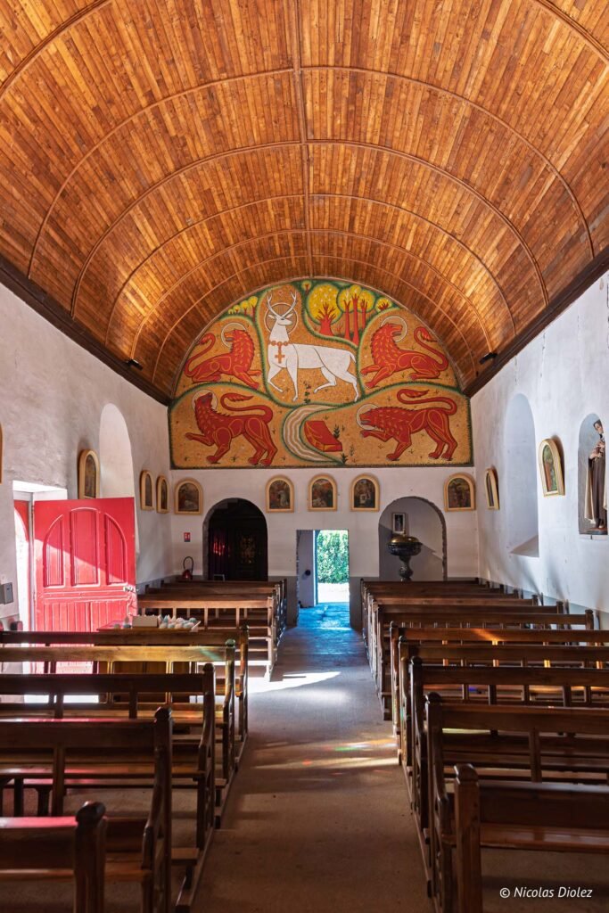 Intérieur Église du Graal : bancs bois, plafond cintré, mosaïque cerf et lions.
