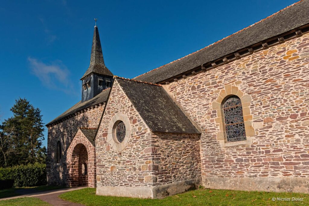 Église du Graal en pierre, avec clocher et vitraux sous un ciel bleu.