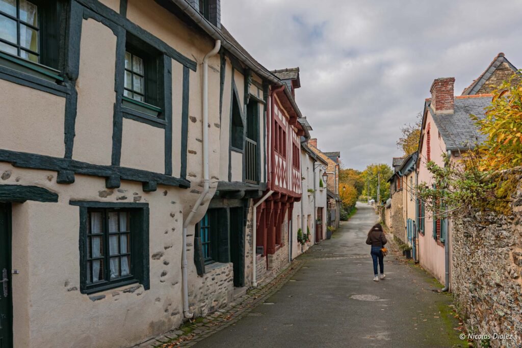 Ruelle pavée à Josselin avec maisons à pans de bois et femme marchant.