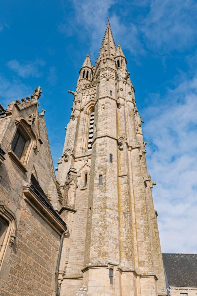 Clocher gothique en pierre à Josselin sous un ciel bleu avec nuages.
