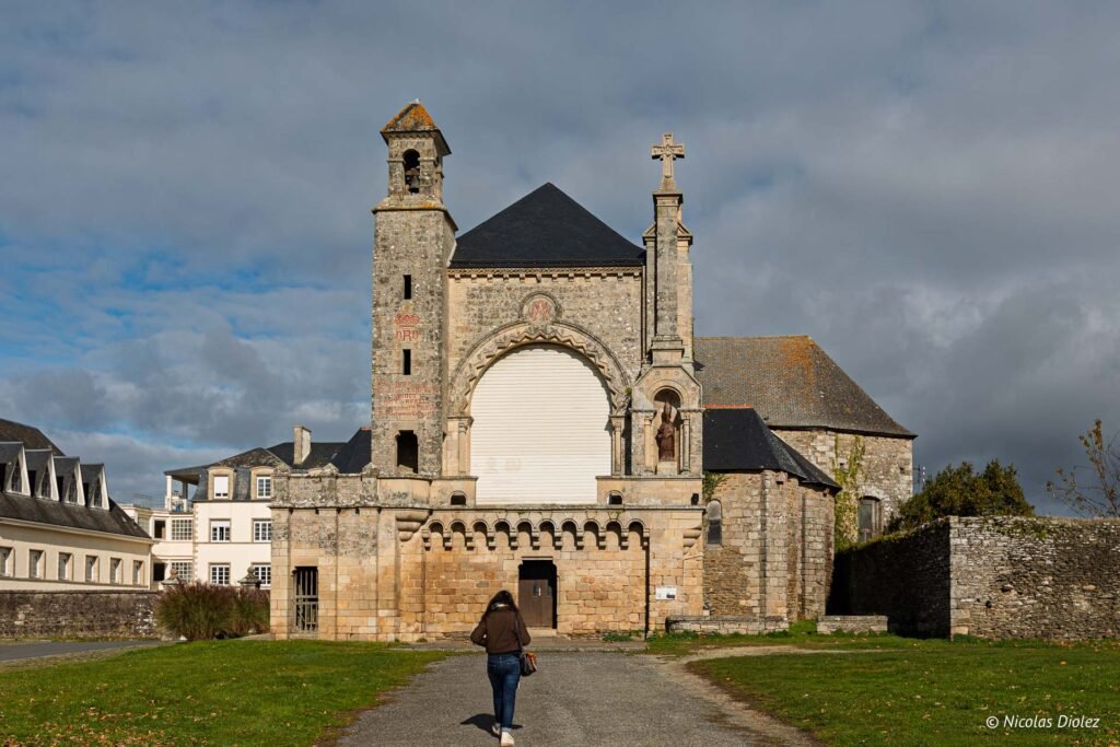 Façade église ancienne en pierre de Josselin avec une femme marchant vers l'entrée.