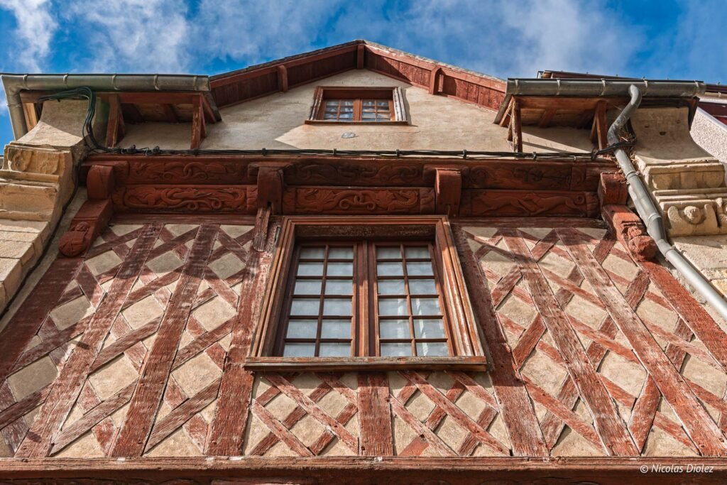 Façade colombages Josselin, encorbellement sculpté, fenêtre à croisillons, ciel bleu.