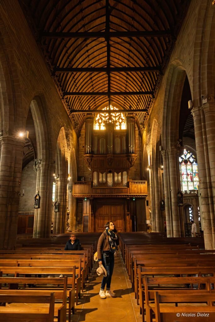Intérieur église Josselin avec orgue, vitraux, et visiteuse près des bancs.