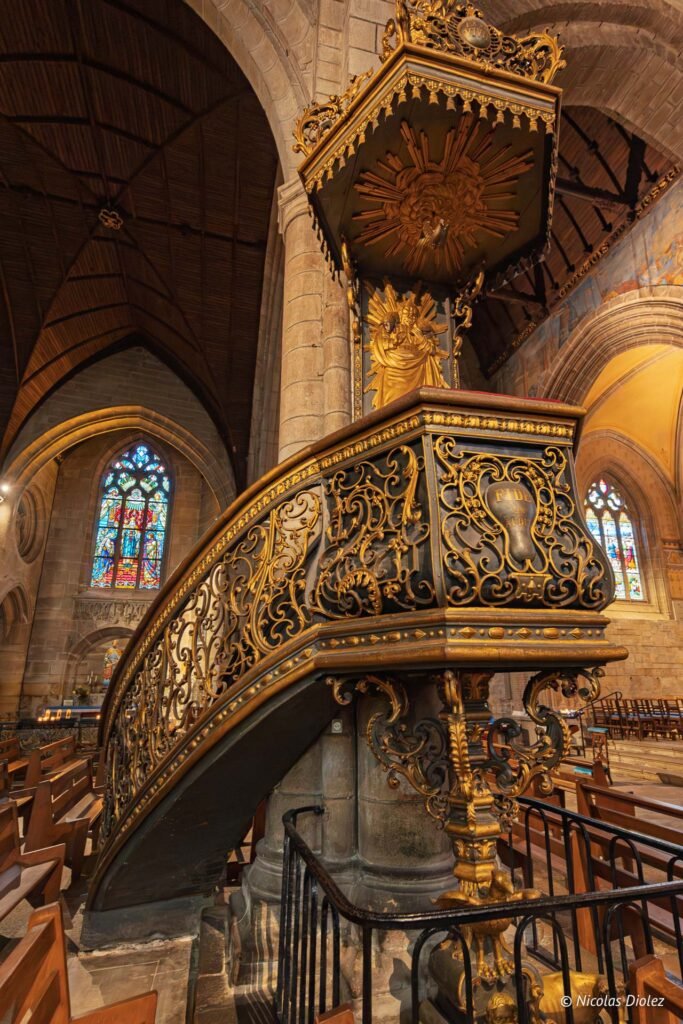 Chaire ornée en fer forgé doré dans une église avec vitraux.