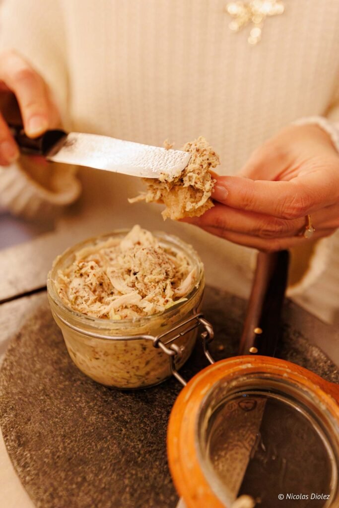 Tartinade de viande au couteau sur pain dans pot en verre.