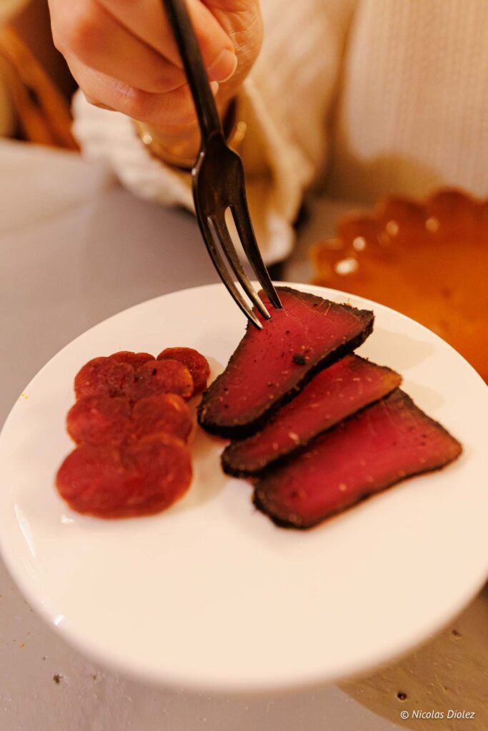 Fourche piquant tranches de viande séchée rouge sur assiette blanche.