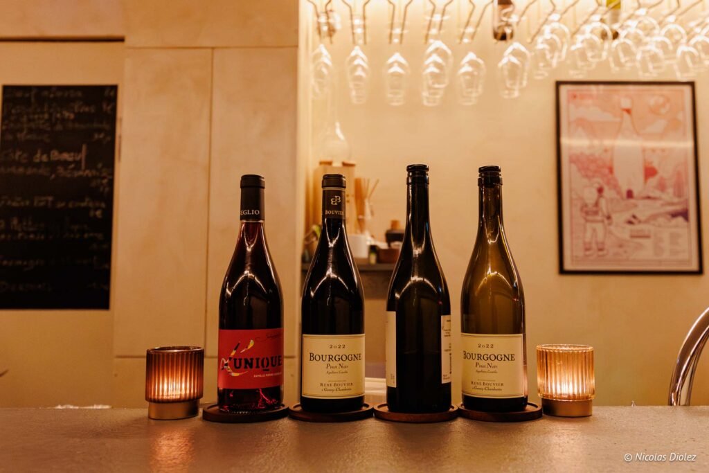 Quatre bouteilles de vin, dont Bourgogne Pinot Noir René Bouvier 2022, sur un comptoir éclairé.