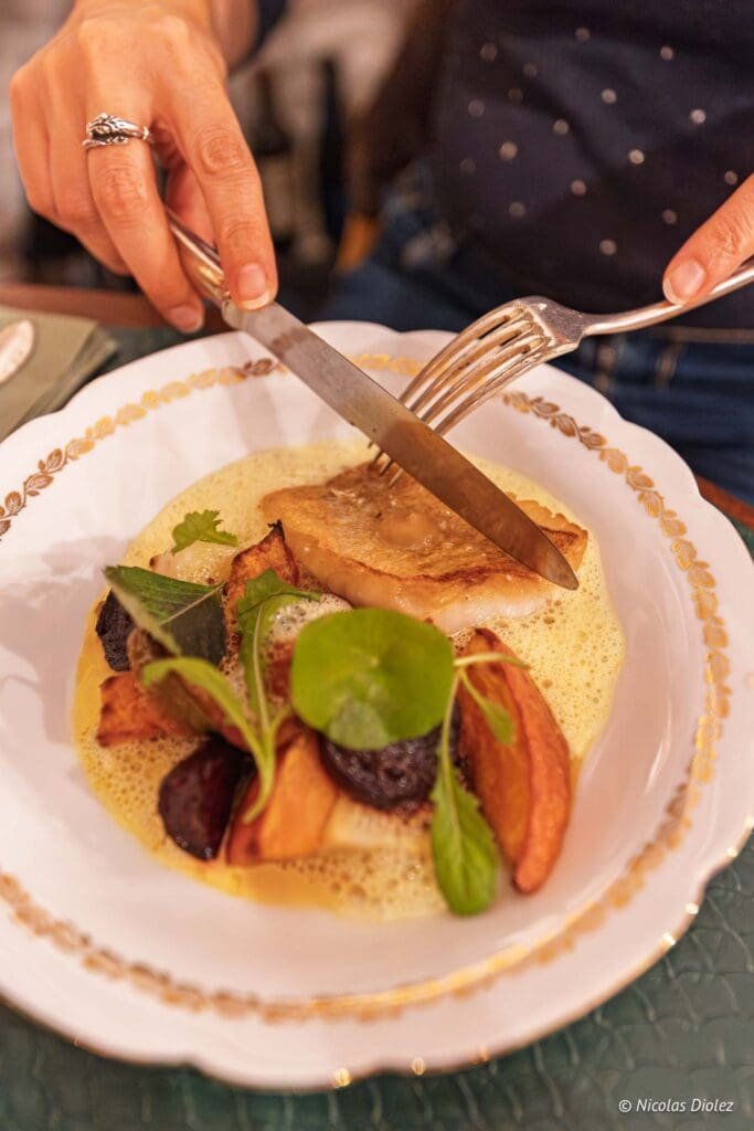 Personne coupant poisson et légumes dans sauce mousseuse avec couteau et fourchette.