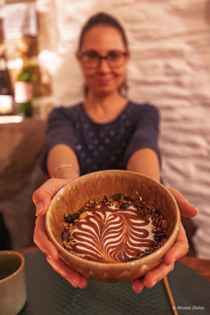 Femme présentant un bol de yaourt décoré de chocolat et de graines.