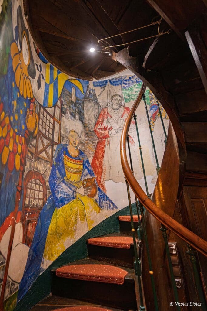 Escalier en colimaçon près d'une fresque murale colorée dans La Maison Cachée.