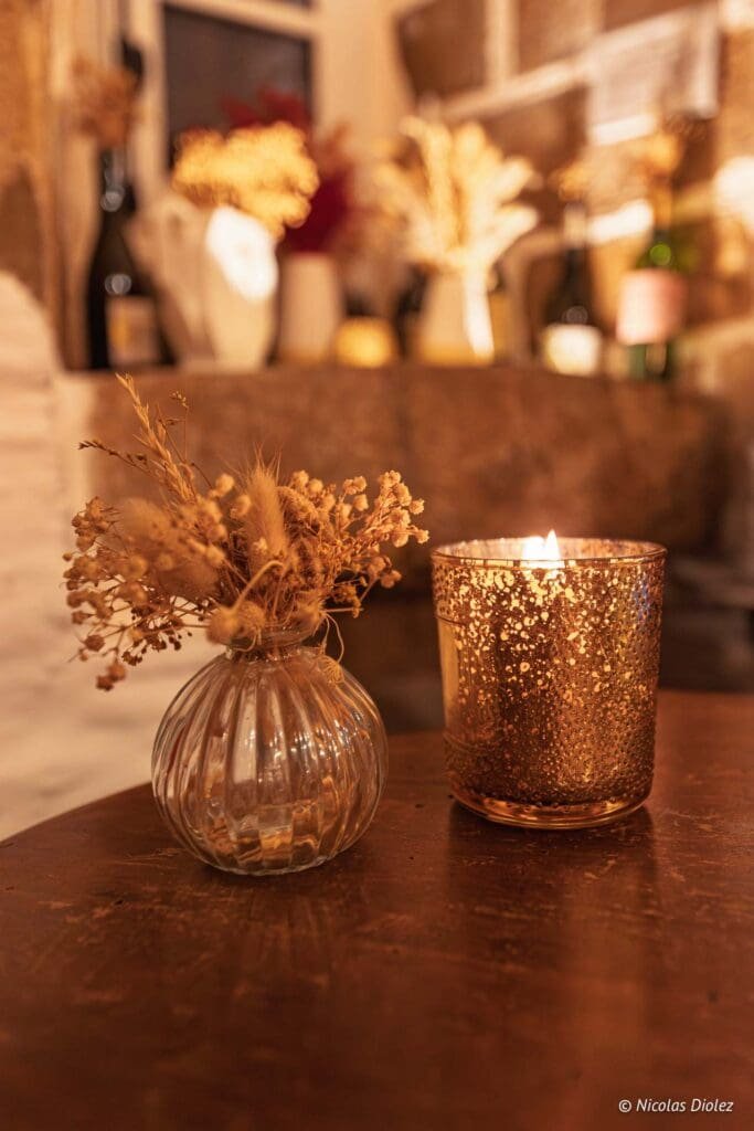 Vase de fleurs séchées et bougie dorée allumée sur une table en bois. © Nicolas Diolez