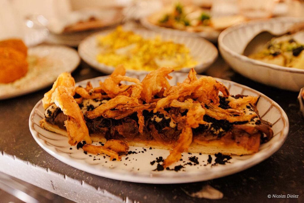 Tartelette garnie d'oignons frits croustillants et miettes noires.