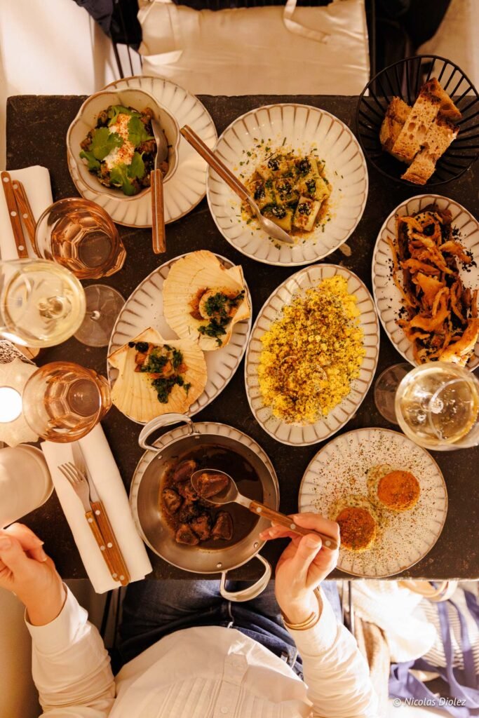 Repas gastronomique avec noix de Saint-Jacques, couscous, et ragoût sur table sombre.