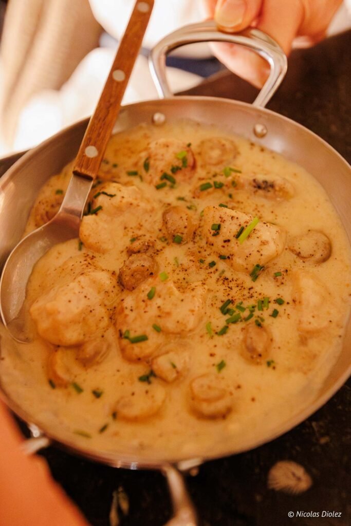 Ris de veau sauce crème et champignons, servi dans une poêle avec cuillère.