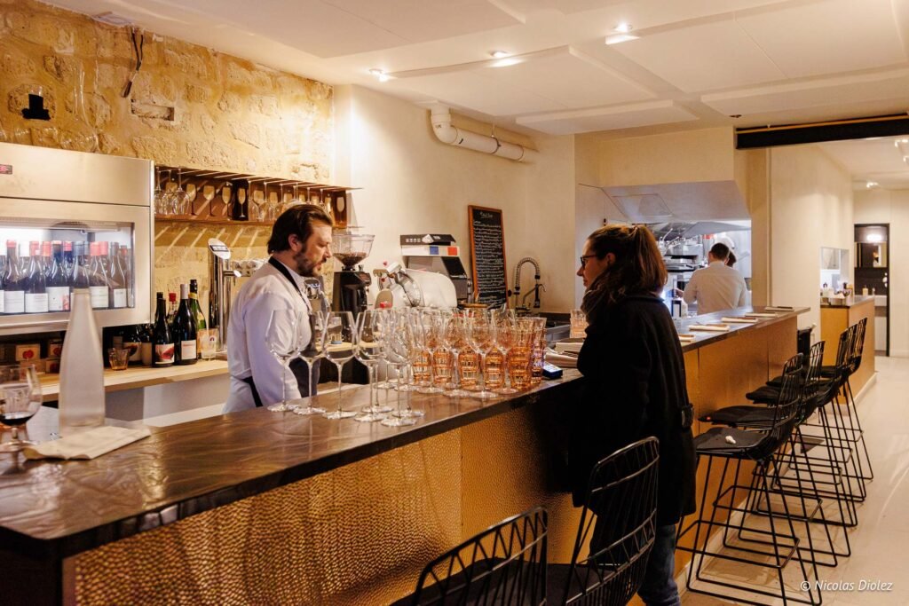 Serveur au bar du Tire-Bouchon Rodier avec cliente et verres à vin.