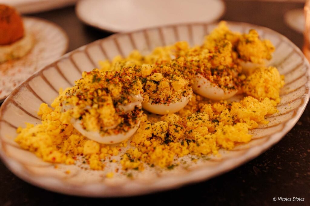 Œufs mimosa émiettés et assaisonnés sur une assiette rayée.