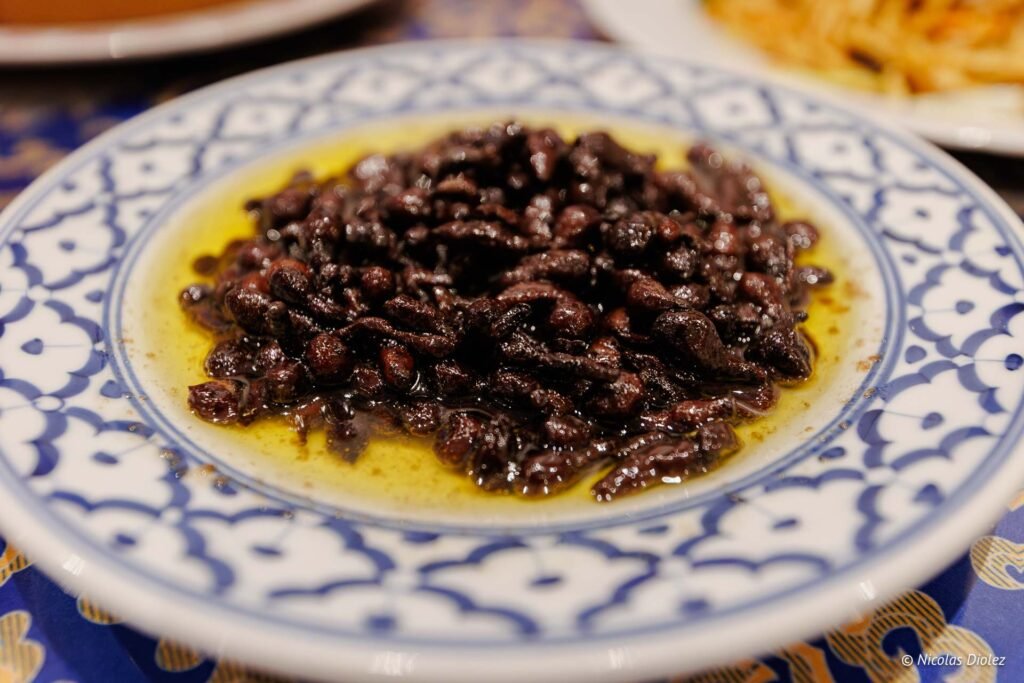 Petits fruits séchés foncés dans l'huile sur assiette décorative bleue et blanche.