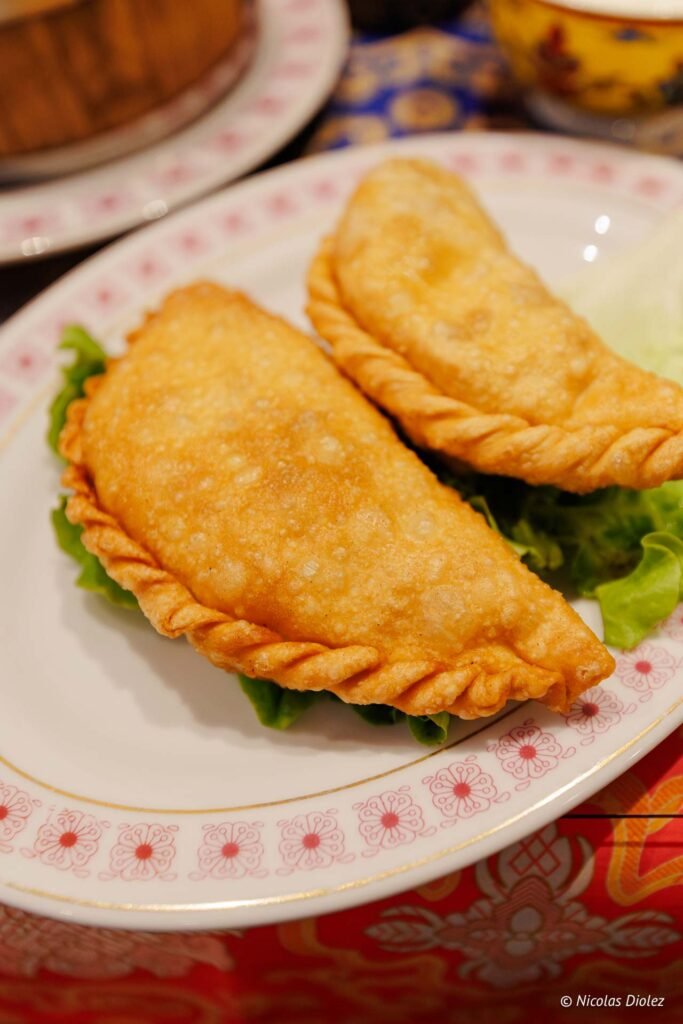 Deux chaussons frits dorés sur une assiette décorée, probablement des Joyaux du Tibet.