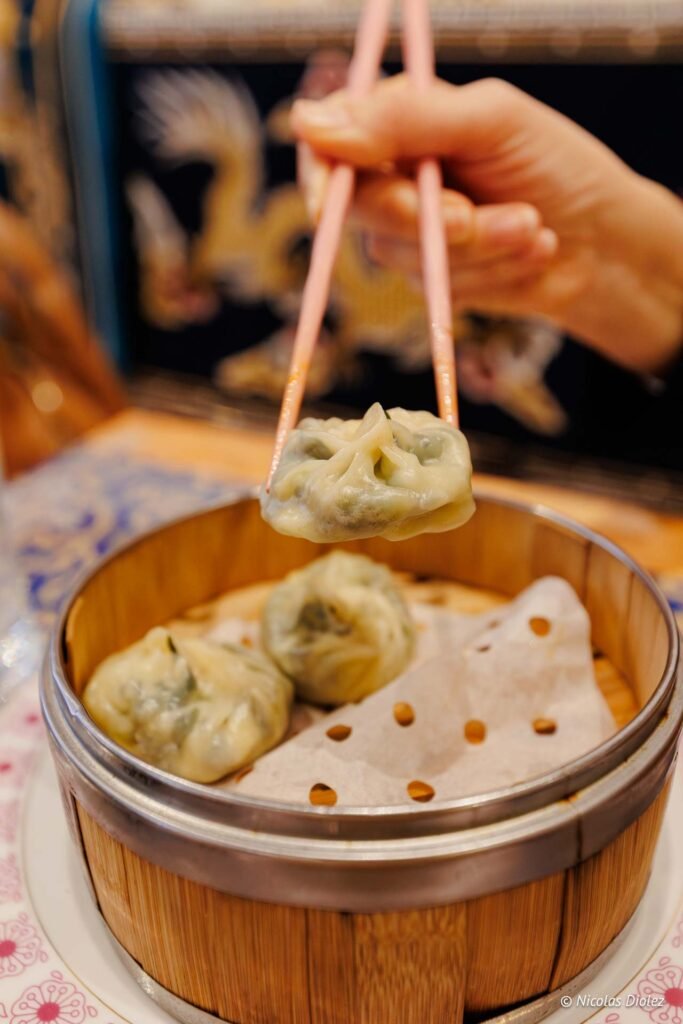 Mains de personne mangeant un momo tibétain avec des baguettes dans un panier vapeur.