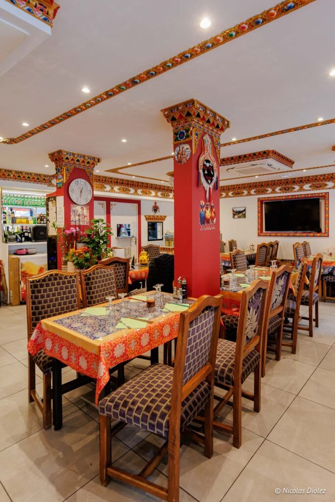 Salle de restaurant tibétain décorée avec des motifs colorés et des tables dressées.