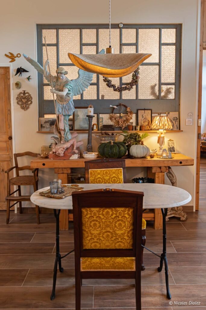 Intérieur rustique avec statue Saint Michel, citrouilles, table marbre et chaise à motifs jaunes.