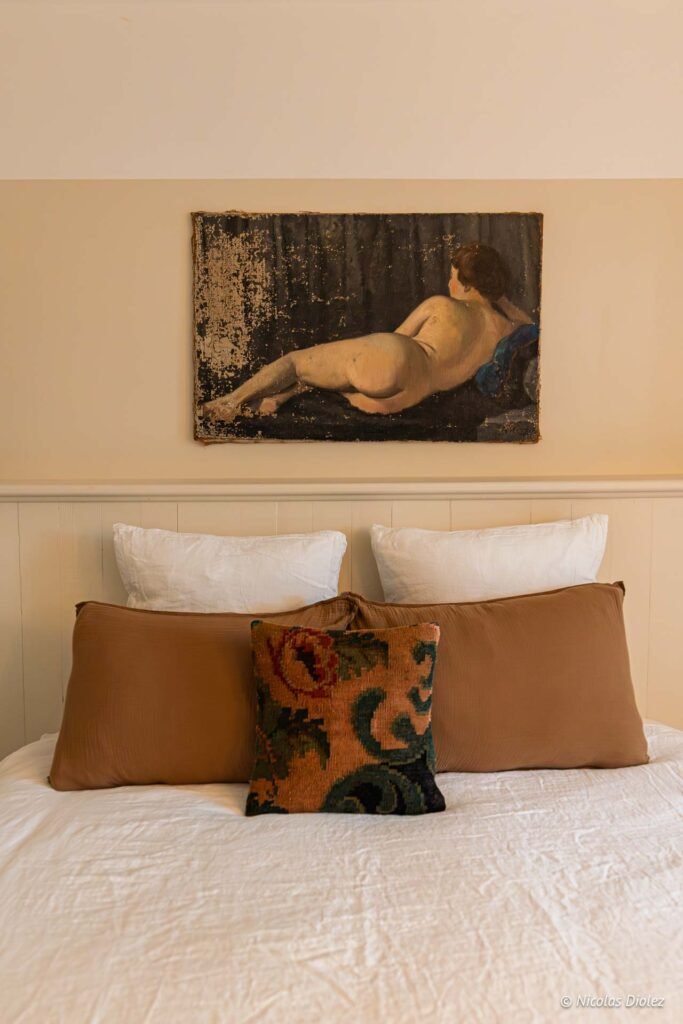 Peinture ancienne d'un nu féminin au-dessus d'un lit avec oreillers.