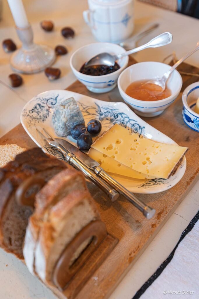 Assiette de fromages (Comté, chèvre cendré) avec raisins, confitures et pain tranché.