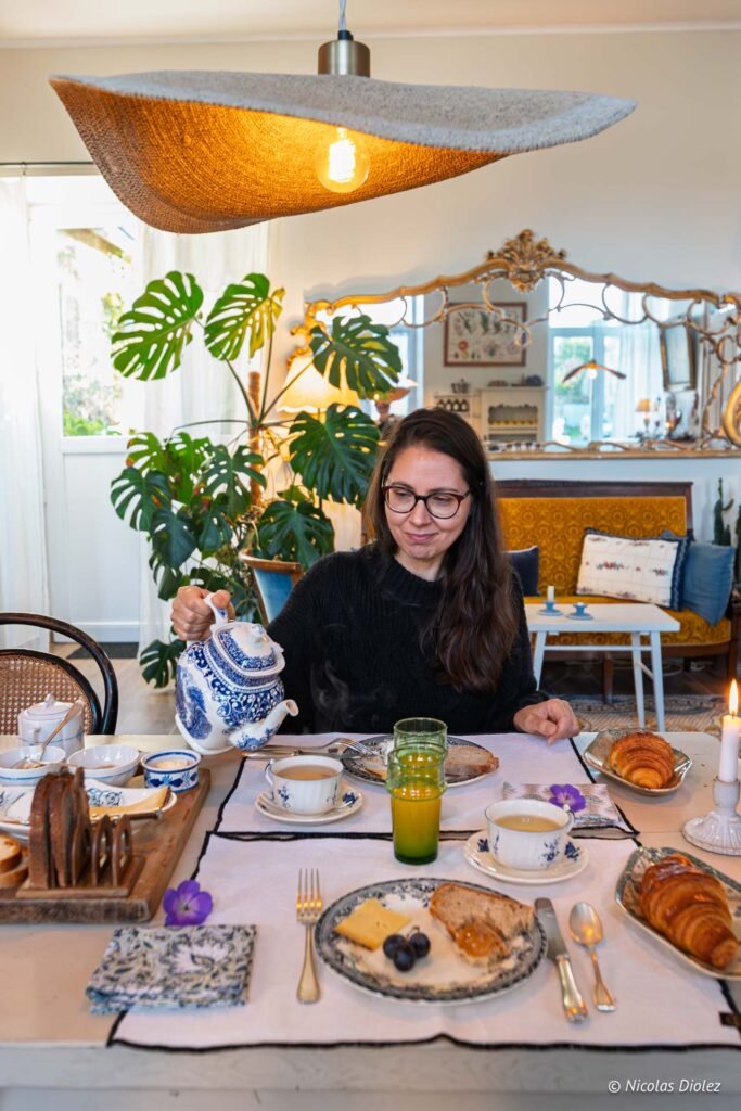 Femme versant du thé d'une théière bleue et blanche lors d'un petit-déjeuner.