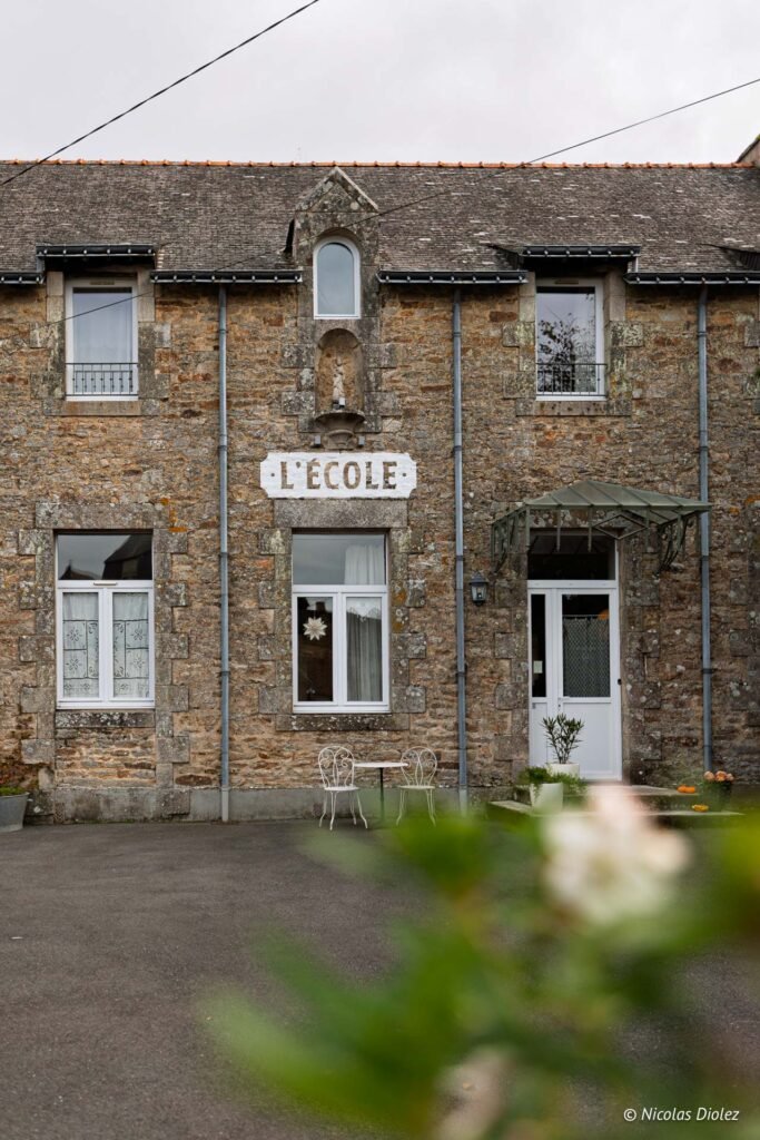 Façade en pierre de l'école ancienne avec inscription "L'ÉCOLE" et porte blanche.
