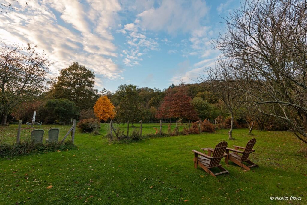 Jardin d'automne avec fauteuils Adirondack et ciel nuageux près du Manoir du Vau d'Arz.