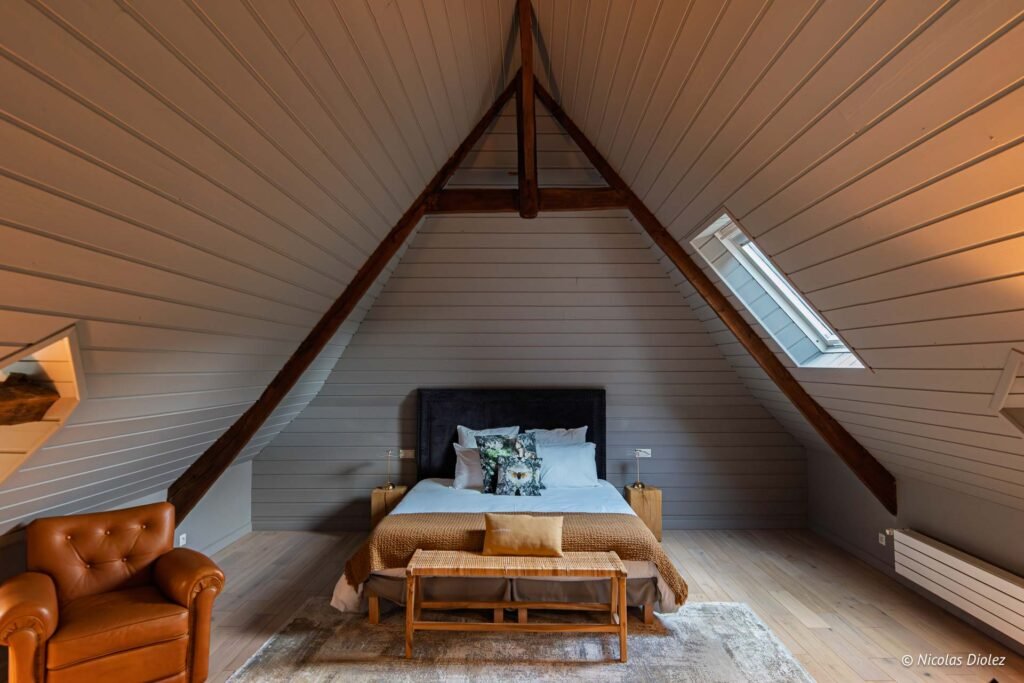 Chambre sous combles mansardée avec poutres apparentes et mobilier moderne.