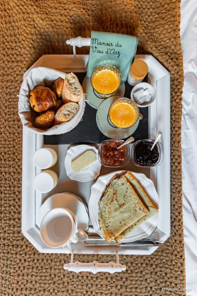Petit-déjeuner Manoir du Vau d'Arz : crêpes, viennoiseries, jus d'orange sur plateau.