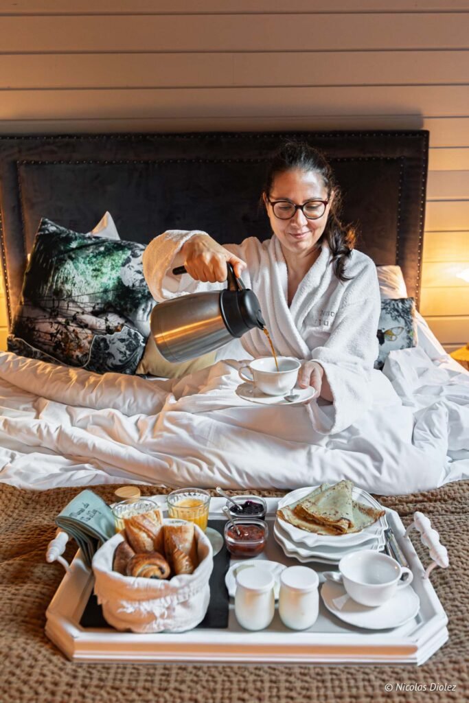 Femme en peignoir versant café au lit avec plateau petit-déjeuner Manoir du Vau d'Arz.