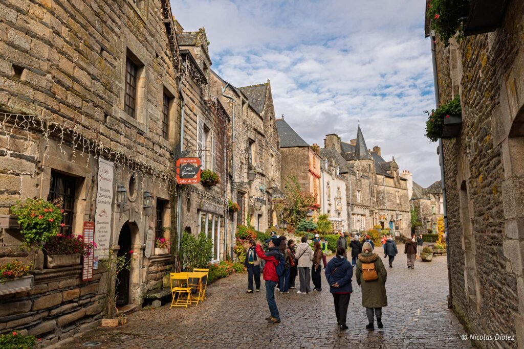 Rue pavée historique à Rochefort-en-Terre avec touristes et enseigne L'Art Gourmand.