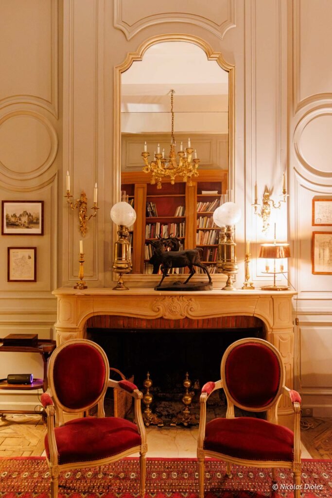 Cheminée luxueuse avec miroirs, chaises velours rouge et sculpture animalière, Château de la Rivière.