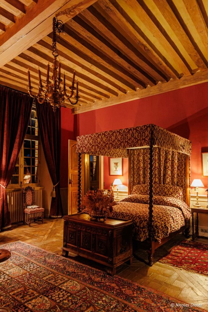 Chambre d'hôtes luxueuse au Château de la Rivière avec lit à baldaquin et poutres apparentes.