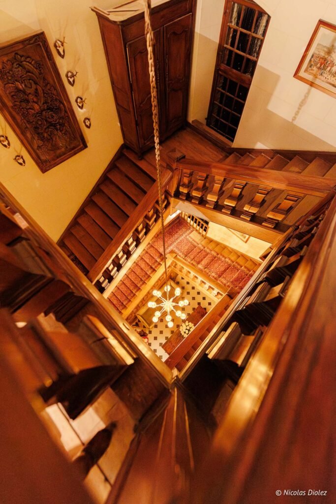 Escalier intérieur en bois du Château de la Rivière vu d'en haut avec lustre.