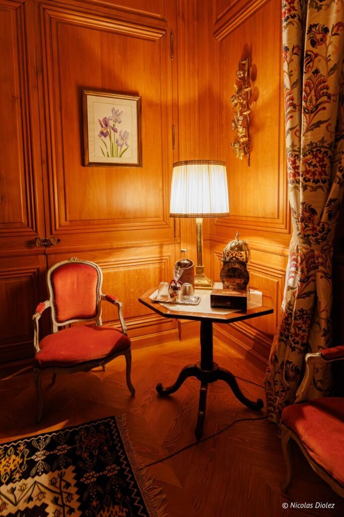 Coin salon boisé avec fauteuil Louis XV, lampe et horloge ancienne.