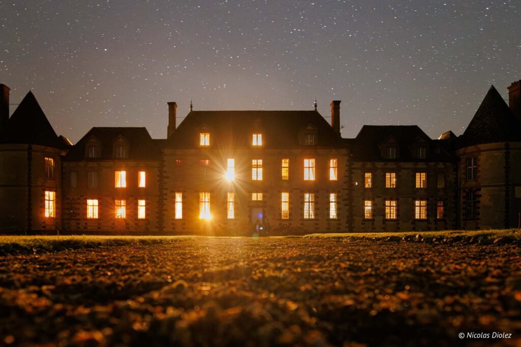 Château de la Rivière illuminé la nuit sous un ciel étoilé, par Nicolas Diolez.
