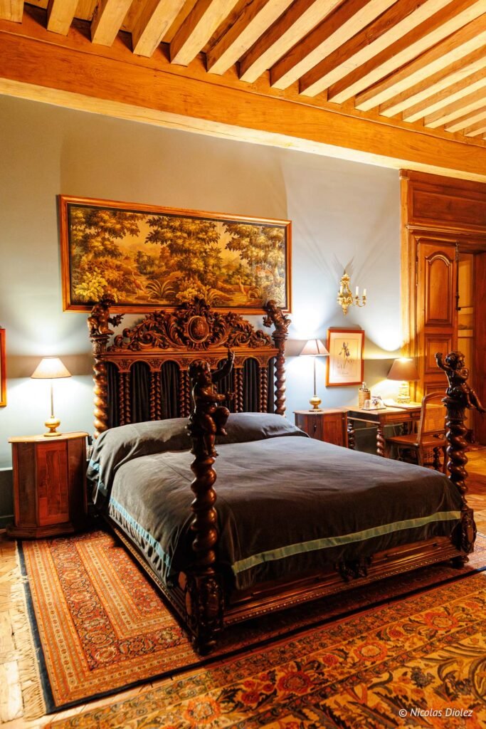 Chambre d'hôtes luxueuse au Château de la Rivière avec lit à baldaquin sculpté.