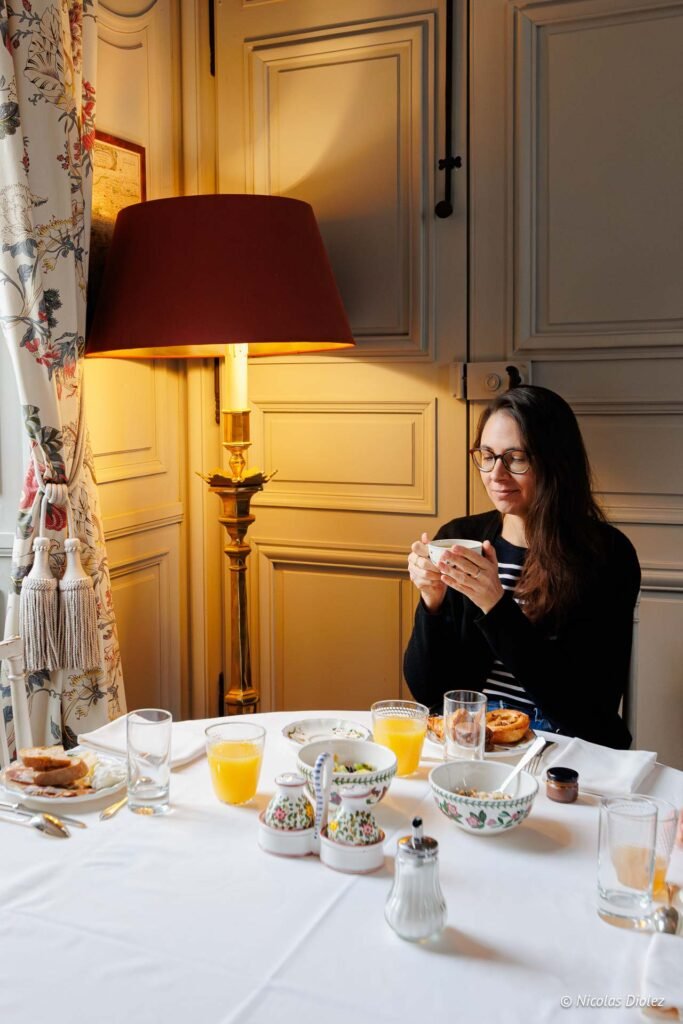 Femme dégustant un petit-déjeuner au Château de la Rivière près d'une lampe.