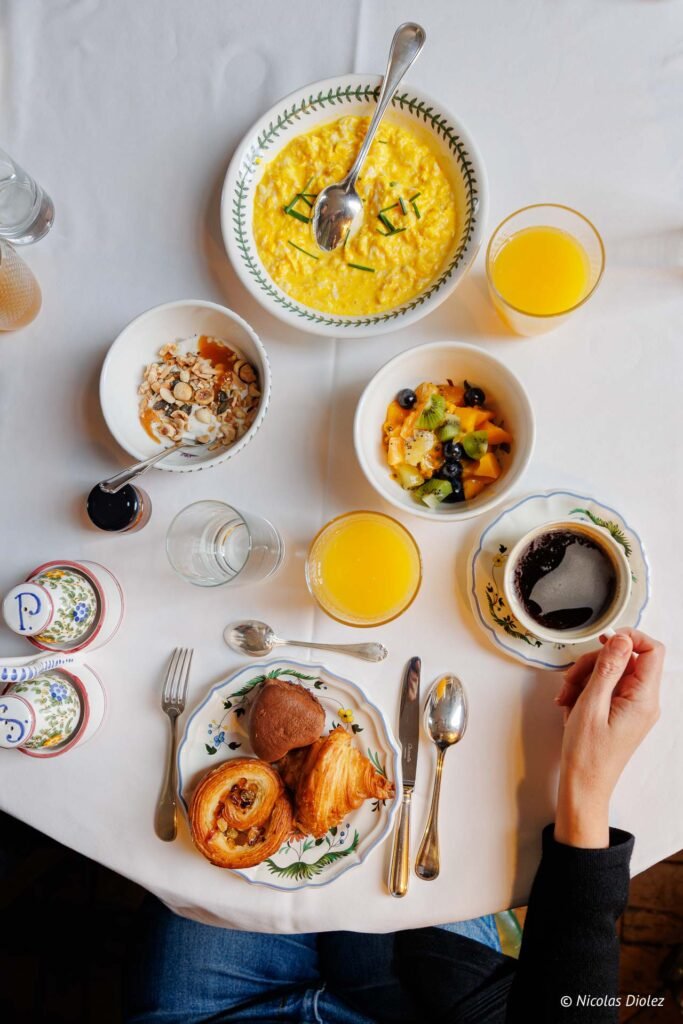 Petit-déjeuner luxueux au Château de la Rivière: œufs brouillés, fruits, viennoiseries, café, jus d'orange.