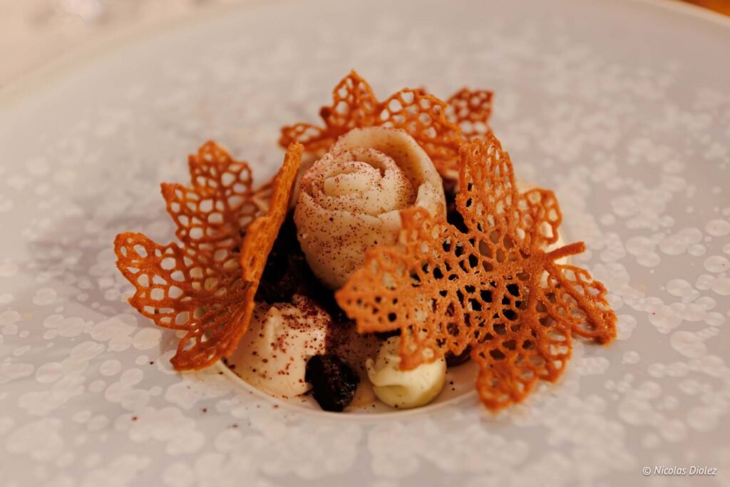 Dessert gastronomique avec tuile dentelle feuille ornementant une crème roulée.