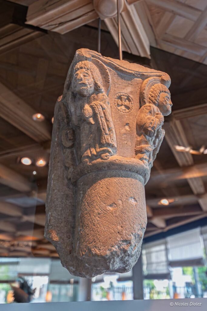 Chapiteau roman sculpté exposé à l'Hôtel d'Angleterre de Châlons-en-Champagne, mettant en valeur des figures religieuses et des croix.
