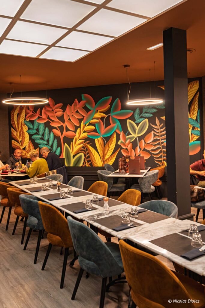 Intérieur du restaurant Le Comptoir de la Licorne à Châlons-en-Champagne avec tables élégantes et fresque murale végétale.