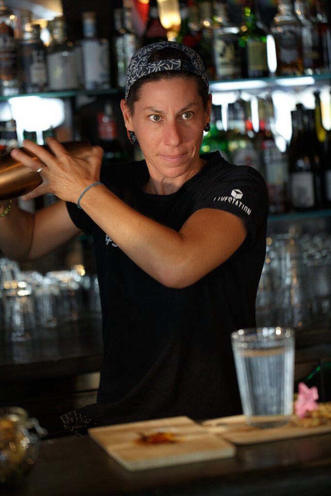 Femme barman professionnelle en plein travail préparant un cocktail derrière le comptoir d'un bar parisien.